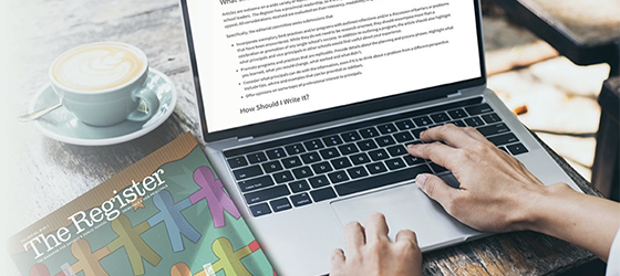 Person typing a story on a laptop with a copy of the Register magazine